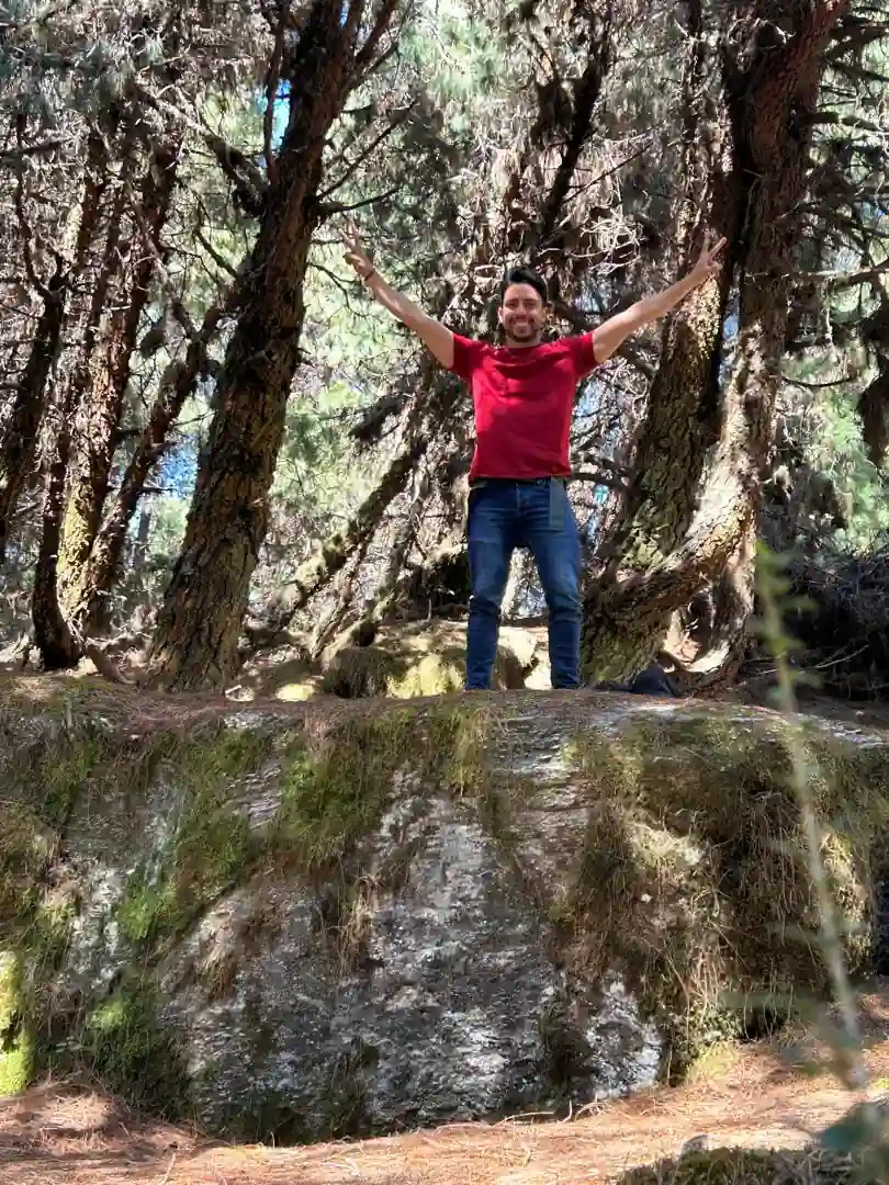 Rafael Cuevas with his arms raised on top of a mossy rock in a pine forest